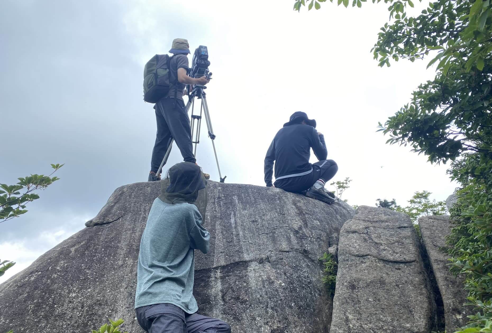 大岩の上から周囲の風景を撮影するスタッフ